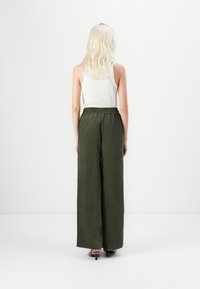 Green ribbed wide-leg pants with an elastic waistband, paired with a white tank top, model viewed from the back against a plain background.