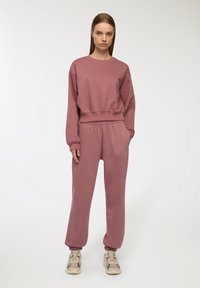Felpa rosa chiaro e pantaloni della tuta coordinati realizzati in un morbido tessuto misto cotone. I pantaloni hanno una cintura elastica e polsini.