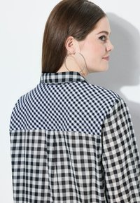 Schwarz-weißes Gingham-Hemd mit kariertem Muster, einem kontrastierenden Karostreifen auf der Rückseite und einem klassischen Kragen.