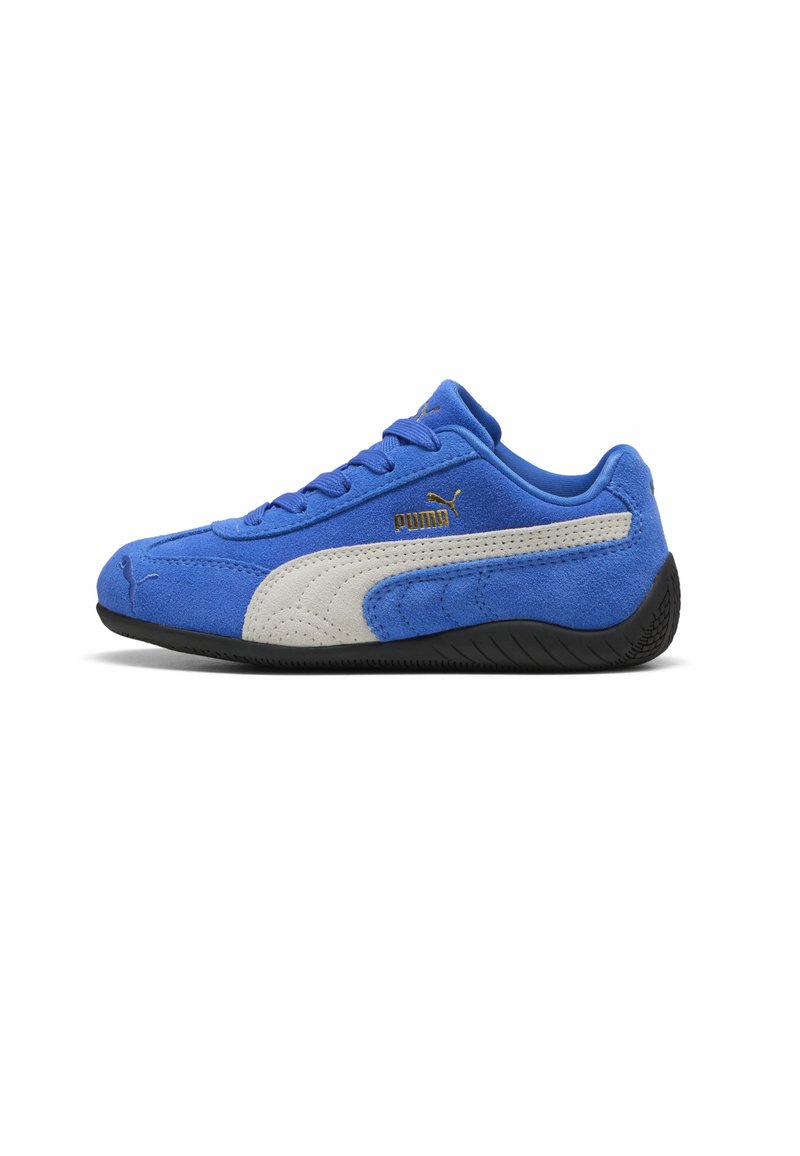 Zapatilla deportiva de gamuza azul con una franja lateral gris, suela de goma negra y cordones azules; presenta un logo dorado de PUMA en el costado.