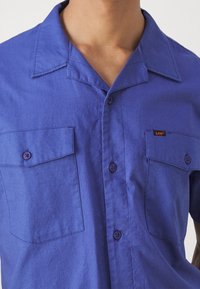 Kortärmad blå skjorta i bomull, med krage, två bröstfickor med knappstängning och en liten märkesetikett.