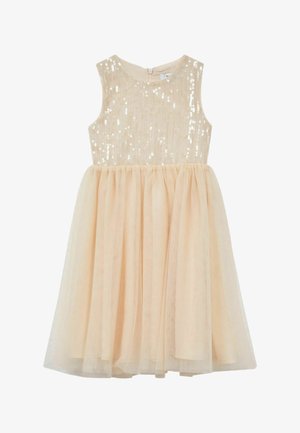 Niña joven con cabello rizado que lleva un vestido beige sin mangas con un cuerpo con lentejuelas y una falda de tul, de pie frente a un fondo blanco sencillo.