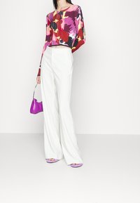 Barevný žebrovaný crop top s dlouhými rukávy, v kombinaci s bílými kalhotami s širokými nohavicemi. Doplněno malou fialovou kabelkou a odpovídajícími sandály.