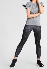 Harmaa urheilupaita, jossa on lyhyet hihat ja hienovaraisia reikiä, yhdistetty mustiin legginsseihin, joissa on valkoisia täpliä, sekä mustiin lenkkareihin.