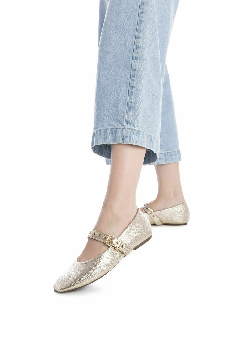 Bailarinas con textura dorada y punta cuadrada, con una correa embellida con tachuelas decorativas, combinadas con pantalones de mezclilla recortados en azul claro.