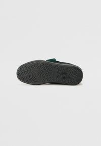 Schoen met rubberen zool, voorzien van een gestructureerde zwarte onderkant en een donkergroene bovenkant met gladde accenten, geschikt voor casual gebruik.