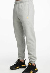 Pantalones de chándal grises hechos de un material suave, con una cintura elástica, bolsillos laterales y un pequeño logo dorado en el muslo.