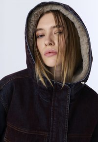 Džínová bunda s kožíškem na kapuci, v tmavě modré a fialové barevné kombinaci, s kontrastním prošíváním a patentními knoflíky.