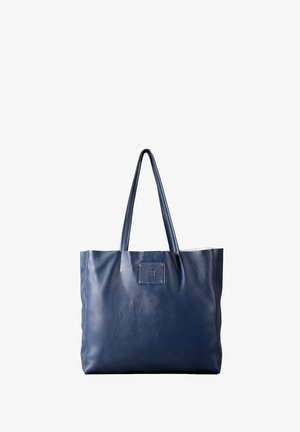Navy blue leather tote bag with two handles, featuring a square logo patch and a textured finish. Open top and spacious interior.
