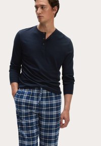Henley de manga larga en color marino con tres botones, combinado con pantalones de pijama a cuadros azules con líneas blancas, cinturilla con cordón y ajuste relajado.