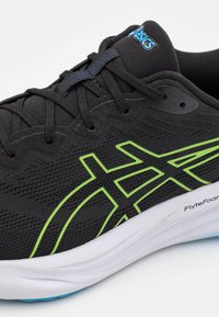 Scarpa sportiva nera con tomaia texturizzata, logo e dettagli verdi, e suola intermedia bianca. Presenta allacciatura tradizionale e colletto imbottito.