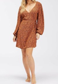 Robe courte orange avec décolleté en V, longues manches bouffantes, design enroulé et motif léopard subtil. Texture de tissu douce, longueur au-dessus du genou.