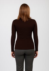 Maglietta marrone a maniche lunghe con un design aderente, caratterizzata da una texture liscia, scollo rotondo e abbinata a pantaloni grigi aderenti.
