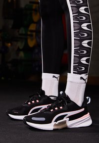 Svarta träningsskor med rosa, vita och grå accenter; mesh och släta material; matchade med svarta leggings med mönstrad sida.