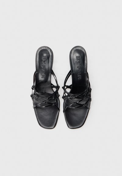 Schwarze Leder-High-Heel-Sandalen mit offenem Zehenbereich, quadratischer Form und überkreuztem Riemendesign. Texturiertes Fußbett mit eingeprägtem Logo.