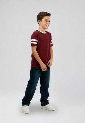 Bordo majica s kratkimi rokavi z belimi črtami, kombinirana s temno modrimi kavbojkami in belimi supergami. Model stoji na nevtralni podlagi.