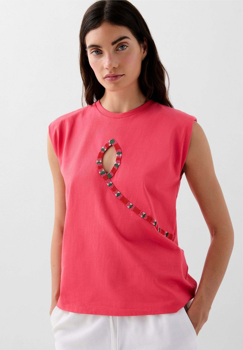 Rosa Baumwoll-Tanktop mit einem einzigartigen Perlenmuster in Rot, Grün und Weiß sowie einem Ausschnitt auf der Vorderseite. Lässige Passform.