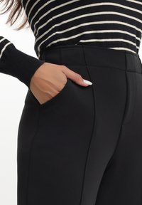 Crne krojene hlače s bočnim džepovima, s glatkom teksturom i elegantnim dizajnom. Pojas je prilagođen i bez šavova.