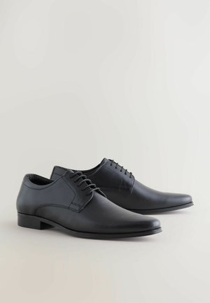 Scarpe eleganti in pelle nera con una superficie liscia e testurizzata, punta affusolata, design con lacci e tacco basso minimalista.