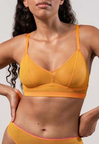 Keltainen bralette, jossa on sileä pinta, ohuiden nauhojen ja kontrastivärisen oranssin reunan kanssa. Tyylissä on yksinkertainen ja moderni ilme, kolmiomainen muoto.