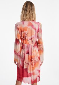 Blumenkleid aus transparenter Stoff, mit einer Mischung aus Pink-, Orange- und Rottönen. Lange Ärmel mit gerafften Akzenten und einem elastischen Taillenbund.