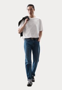 Biały t-shirt, niebieskie dżinsy, czarny pasek i błyszczące czarne buty. Czarna kurtka zarzucona na jedno ramię. Prosty design, luźny krój.