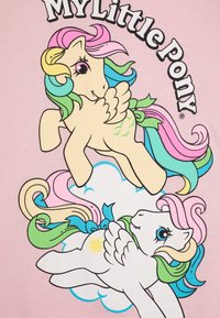T-shirt rose avec deux poneys de dessins animés colorés, l'un crème avec une crinière et des ailes arc-en-ciel, l'autre blanc avec un symbole de soleil, sur un fond de nuages.