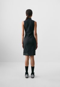 Rochie neagră fără mâneci, cu guler înalt, siluetă ajustată și tiv până la genunchi. Are detalii de cusătură subtile la baza rochiei.