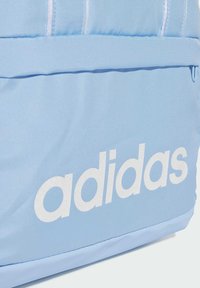 Mochila azul claro hecha de tela duradera con el logotipo blanco de "adidas". Presenta una textura suave y una forma estructurada, con costuras reforzadas.