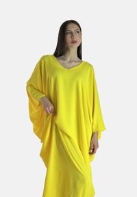 Luźna żółta kaftan o dekolcie w serek, szerokich rękawach typu batwing i teksturowanej tkaninie. Układa się płynnie z miękkiego, lekkiego materiału.