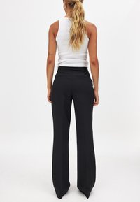 Črne krojene hlače s širokimi nogavicami, ravnim sprednjim delom in stranskimi žepe. Obute s prilagojenim belim topom brez rokavov z rebrasto teksturo.