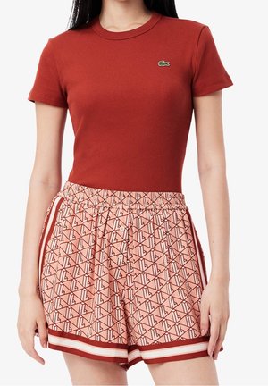 Camiseta roja acanalada combinada con pantalones cortos rosas con estampado. Los pantalones cortos tienen una cintura elástica y rayas contrastantes en el dobladillo.