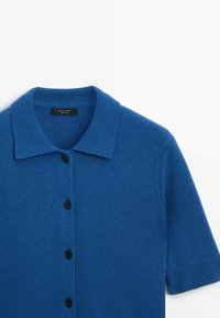 Cardigan tricoté bleu à manches courtes avec col et quatre boutons noirs sur le devant, sur fond blanc.