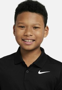 Svart polo skjorta gjord av andningsbart tyg, med en vit Nike-logotyp på vänster bröst och en klassisk krage med knappar.