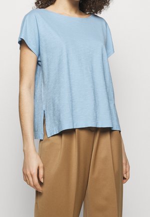 Helles blauen Kurzarmshirt mit lockerem Schnitt, seitlichen Schlitzen, runder Ausschnitt und glatter, weicher Textur. Kombiniert mit braunen Hosen.