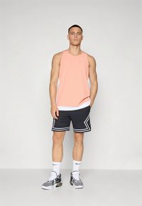 Hele roosa varrukateta sportlik särk, mustad lühikesed püksid valgete aktsentidega ja spordijalatsid. Omaduseks on võrgutekstuur ja logoga detail.