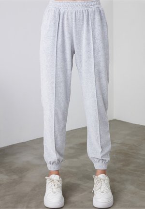 Lys grå fleece joggebukser med elastisk talje og manchetter, båret med hvide sneakers på betongulv indendørs.