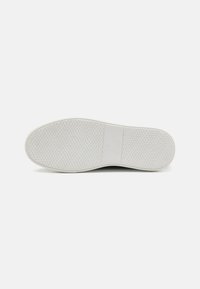 Hvit sneakersåle med en teksturert gummioverflate med runde grep og logodetalj i midten. Glatte kanter og minimalistisk design.