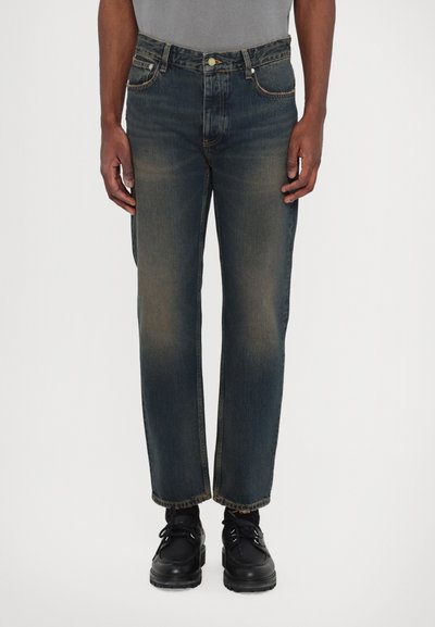 Mørkeblå denimjeans med lige pasform, falmet detaljer, fem lommer og knaplukning, parret med sorte sko.