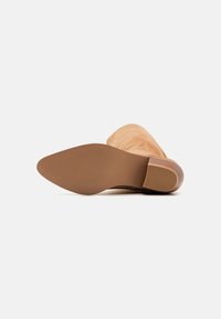 Stivaletto in suede beige con tacco, punta rotonda, parte superiore texturizzata e suola in gomma marrone. Il tacco leggermente curvato arricchisce il design.