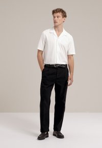 Camisa blanca de manga corta con botones, de tela texturizada, combinada con pantalones negros, que cuentan con un cinturón y zapatos negros tipo mocasín.