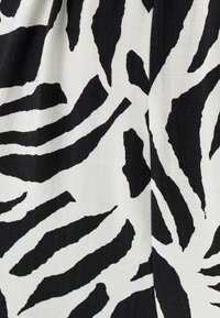 Zwart-witte stof met een zebraprint en een textuurrijke oppervlakte. De strepen zijn onregelmatig en gedurfd, wat een opvallend contrast creëert.