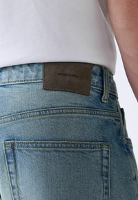 Vervaagde blauwe denim jeans met een gestructureerde bruine leren patch met het label "DENIM SUPPLY" op de achterkant, met een klassiek vijfzakken ontwerp.