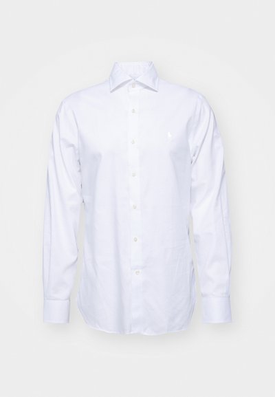 Chemise blanche à manches longues en coton. Elle présente un col pointu et un petit logo brodé sur la poitrine. Texture lisse.