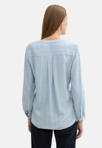 Hellblause Langarmbluse aus weichem Stoff, mit vertikalen weißen Streifen, einem runden Ausschnitt und geknöpften Manschetten.