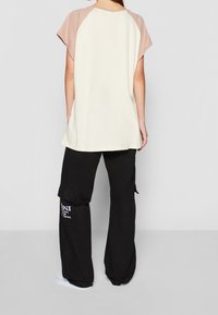 Avslappnad topp med beige raglanärmar, krämfärgad kropp; matchat med vida svarta cargobyxor med sidofickor och vitt textdetalj.