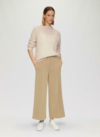 Hellrosa, gerippter Strickpullover mit Rundhalsausschnitt, kombiniert mit beigefarbenen Caprihosen. Die Accessoires umfassen weiße Sneakers.