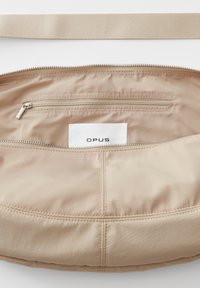 Borsa in tessuto beige con una superficie liscia, dotata di chiusura zip, tasca interna e un'etichetta bianca impressa con "OPUS."