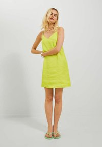 Vestido sin mangas de color verde lima con una superficie texturizada y escote en V, combinado con sandalias verde. Diseño minimalista con un ajuste casual.