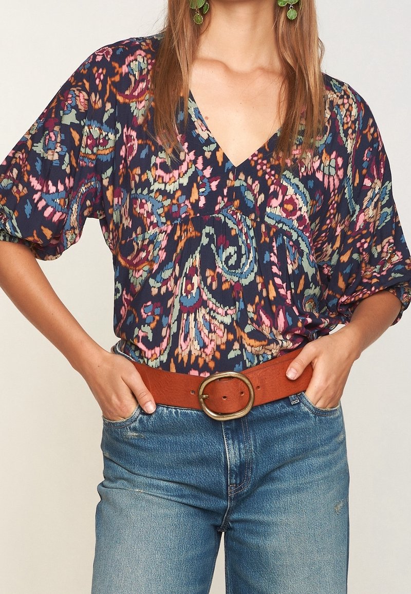 Blouse bleu marine à motifs floraux avec un col en V, des manches courtes et une coupe décontractée, associée à un jean bleu taille haute et une ceinture marron.